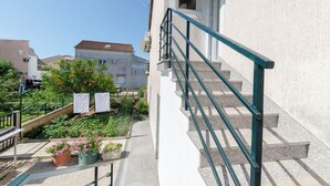Un immeuble résidentiel avec un escalier, un jardin agrémenté de plantes en pot et un ciel d’un bleu éclatant.