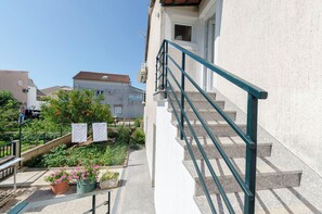 Ein Wohngebäude mit Treppe, einem Garten mit Topfpflanzen und blauem Himmel.