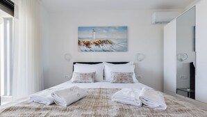 Een hotelkamer met een bed, een schilderij van een vuurtoren, een grote spiegel en een raam met gordijnen.