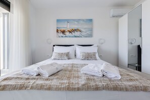 Ein Hotelzimmer mit Bett, einem Gemälde von einem Leuchtturm, einem großen Spiegel und einem Fenster mit Vorhängen.