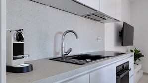 Een moderne keuken met een ingebouwde espressomachine, een roestvrijstalen spoelbak en een flatscreen televisie boven de werkruimte.