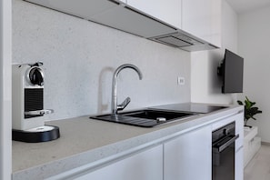Eine moderne Küche mit einer integrierten Espressomaschine, einem Edelstahl-Spülbecken und einem Flachbildfernseher über der Arbeitsfläche.