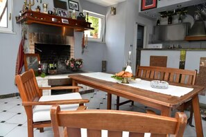 A dining area with a wooden table and chairs, a fireplace, and a kitchen area with a TV. - House Postira Horizon (Postira)
