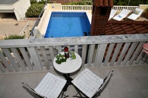 A balcony with a pool, white cushioned chairs, a small table with a bottle and glass, and a white railing. - House Postira Horizon (Postira)
