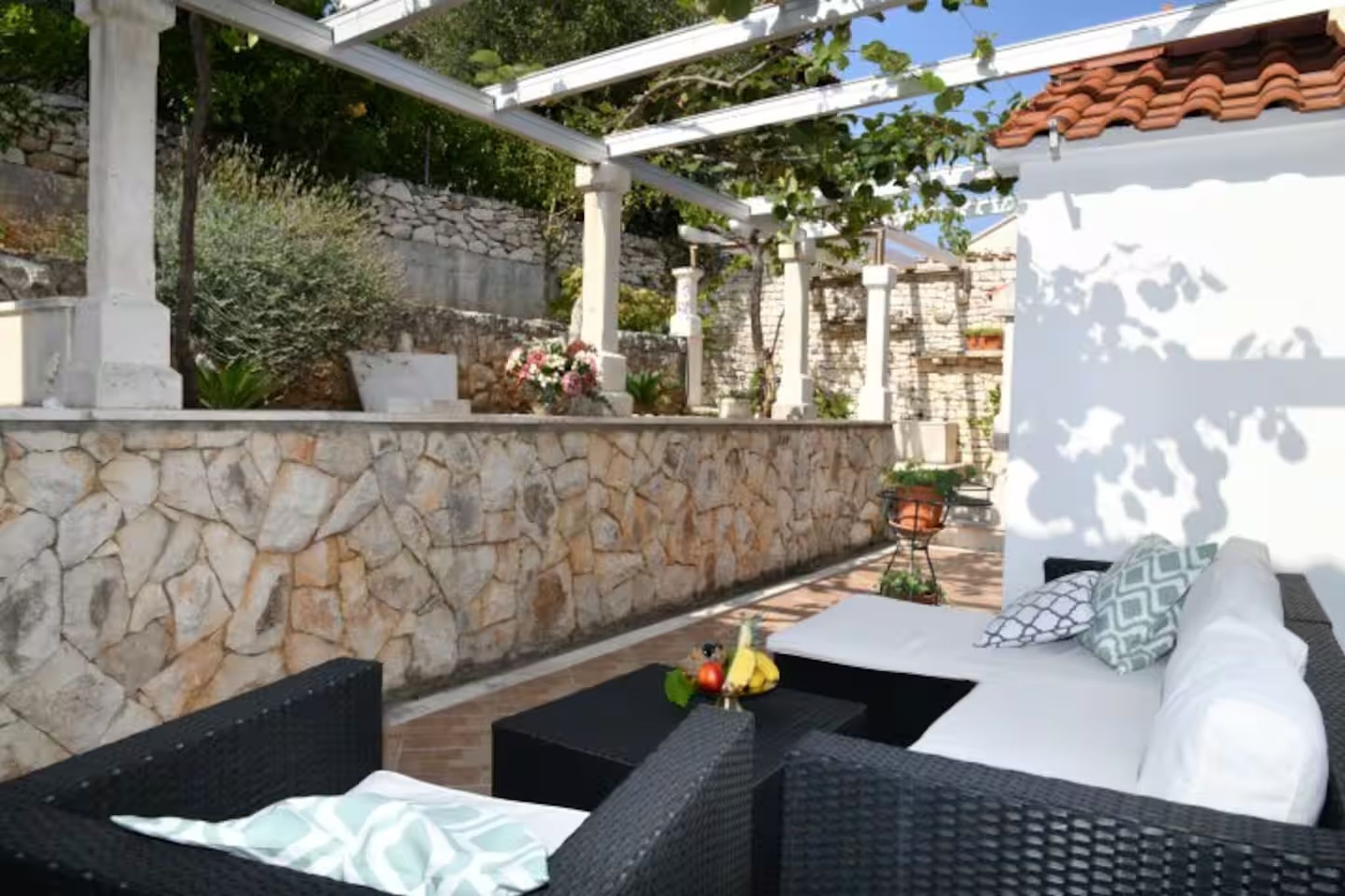 An outdoor seating area with wicker furniture, a stone wall, and a pergola.