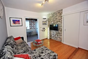 A living room with a sofa, a glass coffee table, a TV, and a stone wall. - House Postira Horizon (Postira)