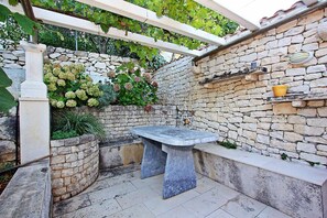 A stone wall with a built-in bench, a pergola with vines, and a stone shelf with a pot. - House Postira Horizon (Postira)