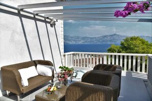 A balcony with wicker furniture, a glass table, and a view of the sea and mountains. - House Postira Horizon (Postira)