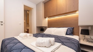 Habitación de hotel con cama, cabecera de madera, mesita de noche y puerta que da a otra habitación.