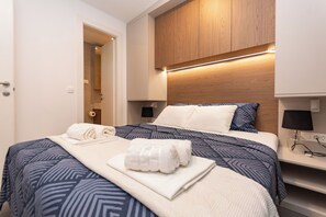 Ein Hotelzimmer mit einem Bett, einem hölzernen Kopfende, einem Nachttisch und einer Tür zu einem anderen Raum.