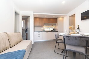 Eine moderne Küche mit Holzausbau, ein Essbereich mit Tisch für zwei Personen und ein Sofa im Wohnbereich.