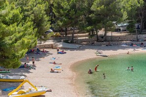 Ein Strand mit badenden Menschen, Booten und einer Steinmauer.