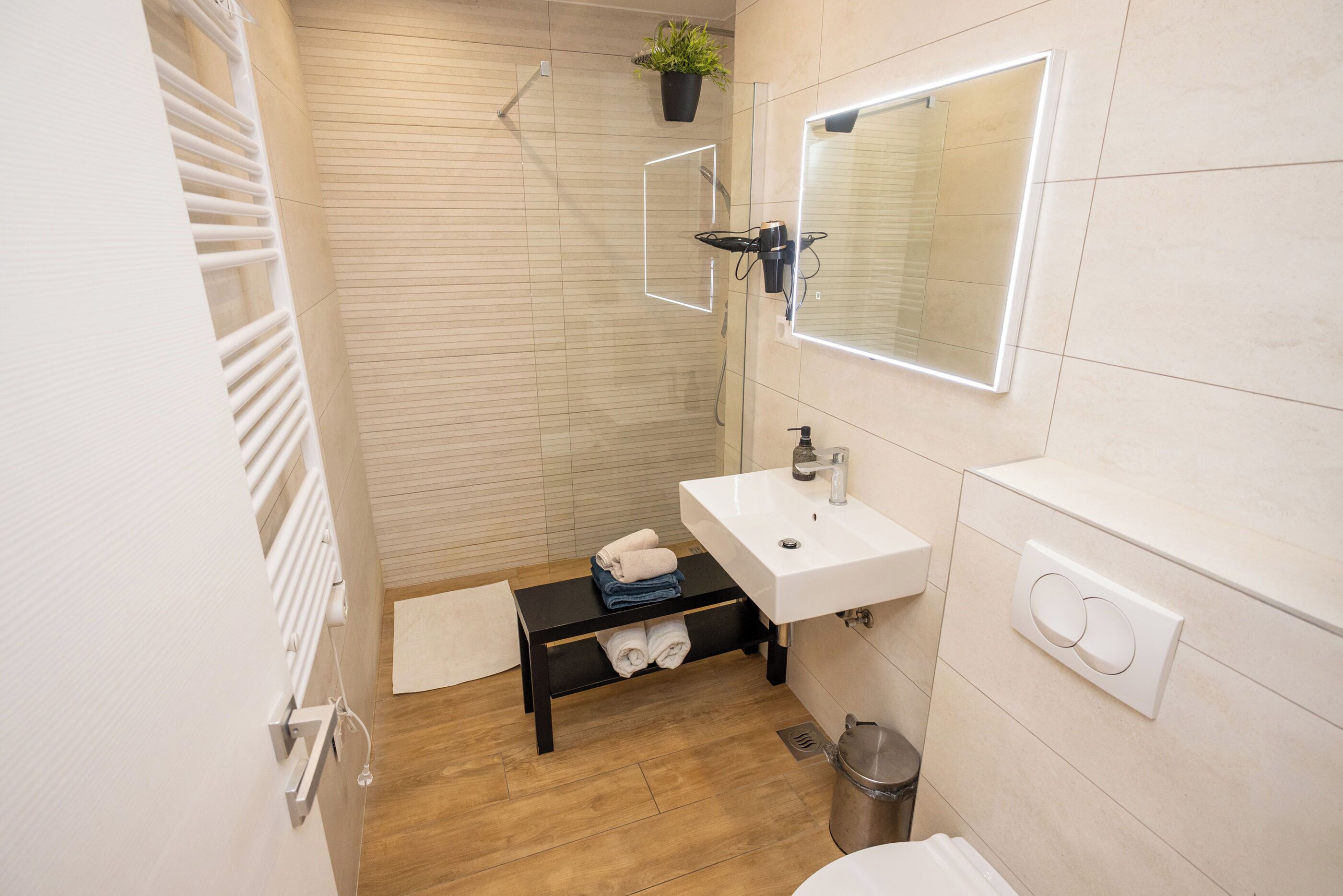 Un baño con un lavamanos blanco, un espejo, toallero, ducha y un estante pequeño con toallas.