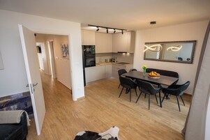 Una cocina moderna con electrodomésticos integrados, un comedor con mesa y sillas, y un espejo grande en la pared.
