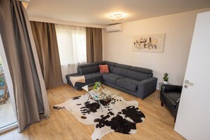 Ein modernes Wohnzimmer mit einem grauen Sofa, einem Glastisch, einem Kuhfellteppich und einem Gemälde an der Wand.