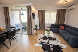 Ein modernes Wohnzimmer mit einer Couch, einem Glastisch, einem Essbereich mit Stühlen und einer Schiebetür zu einem Außenbereich.