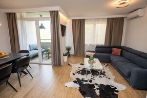 Una sala de estar moderna con un sofá, una mesa de centro de vidrio, una zona de comedor con sillas y un gran ventanal corredizo que da a un espacio exterior.