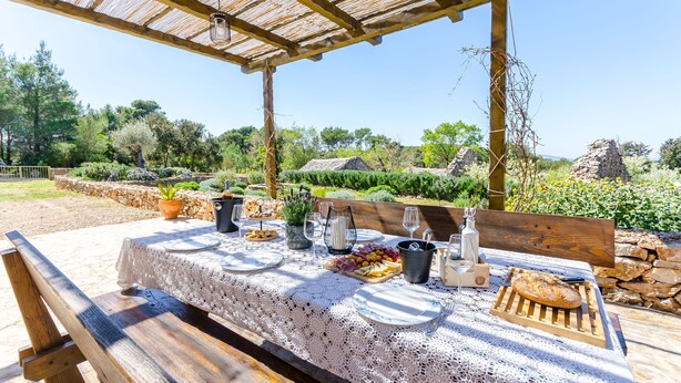 An outdoor dining area with a table set for two, a grill, and a view of the surrounding landscape. - House Bilusic (Jelsa)