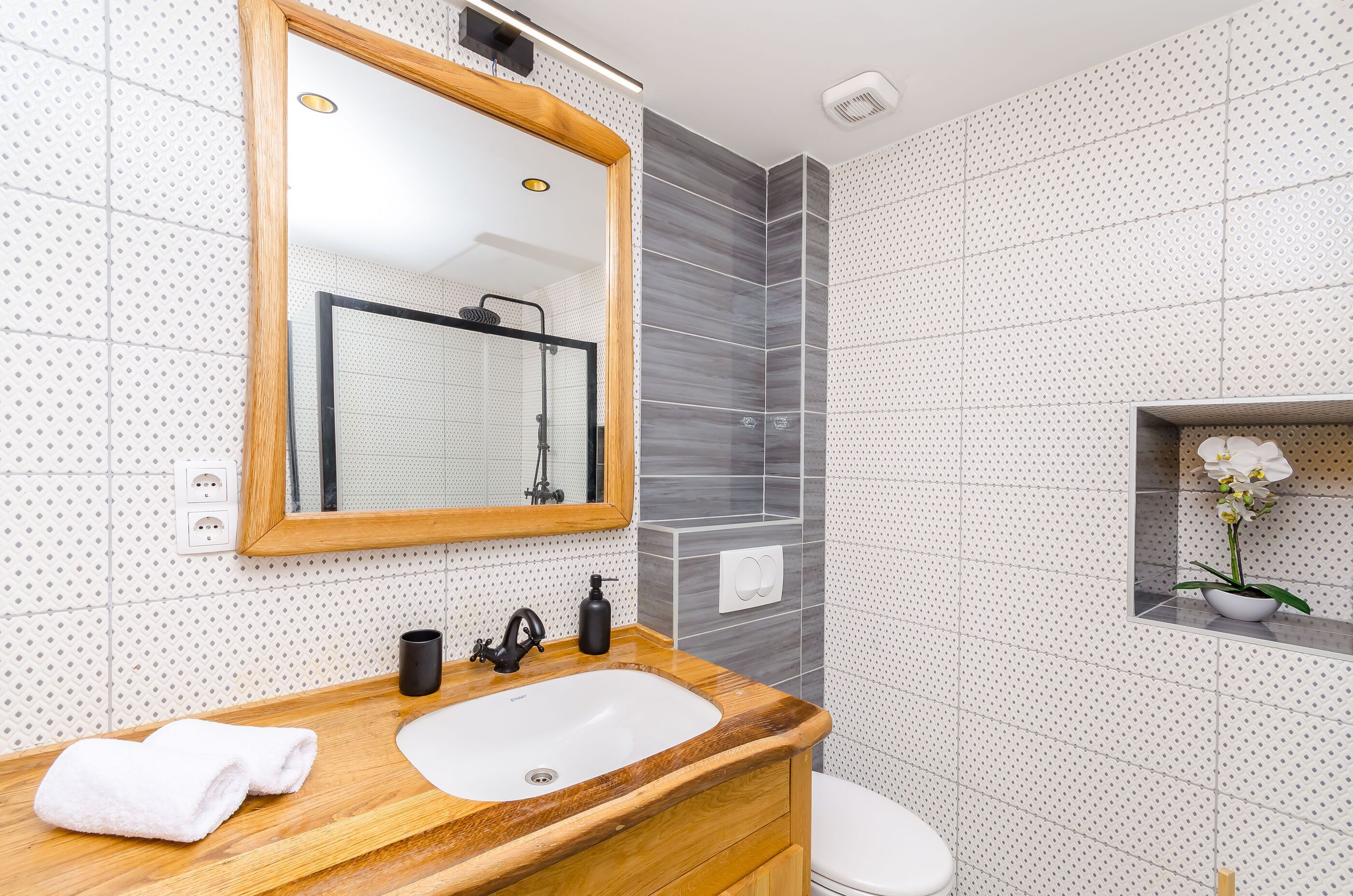 A modern bathroom with a wooden vanity, white sink, and a mirror.