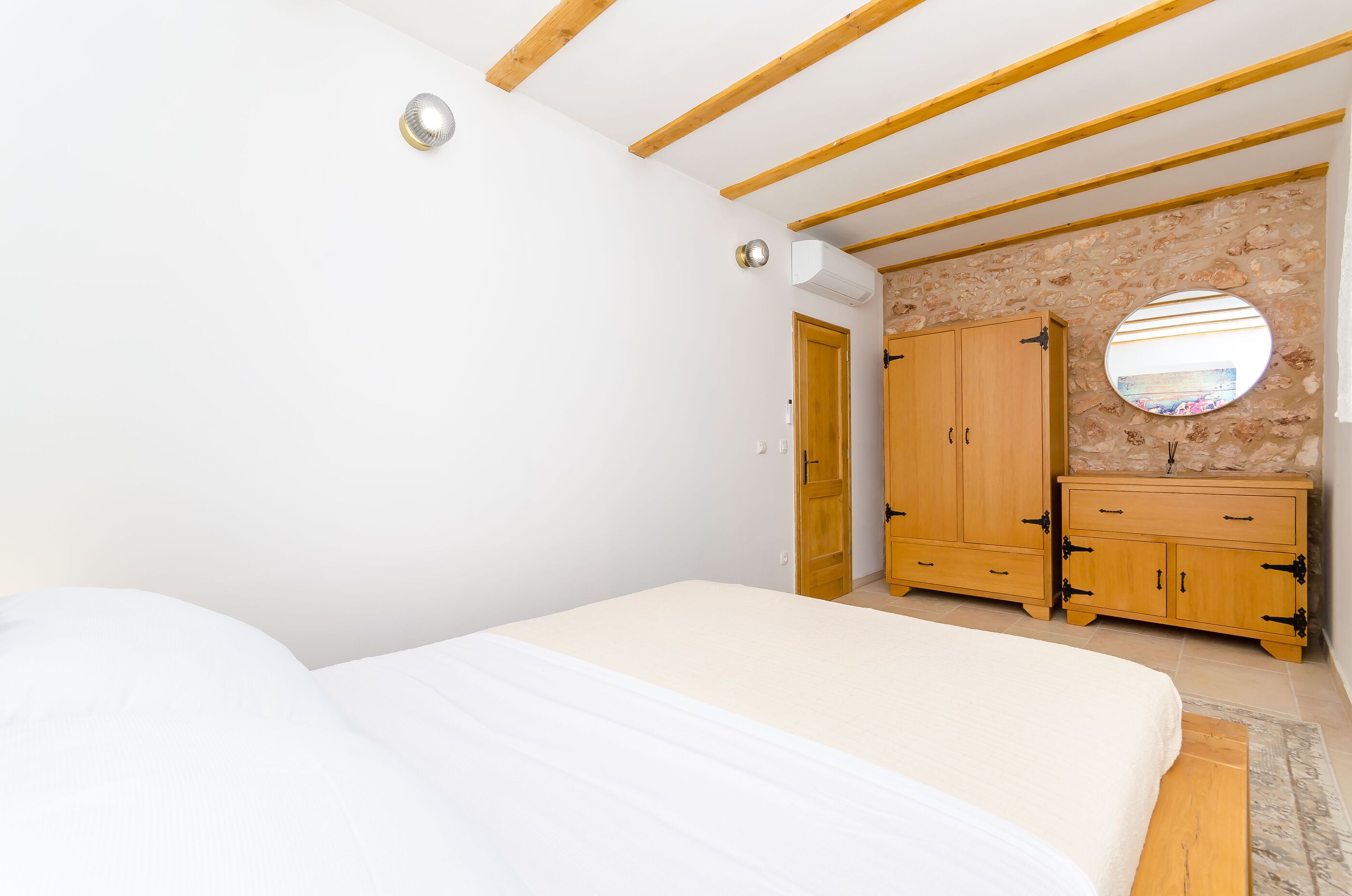 A bedroom with a bed, wooden wardrobe, and a round mirror.