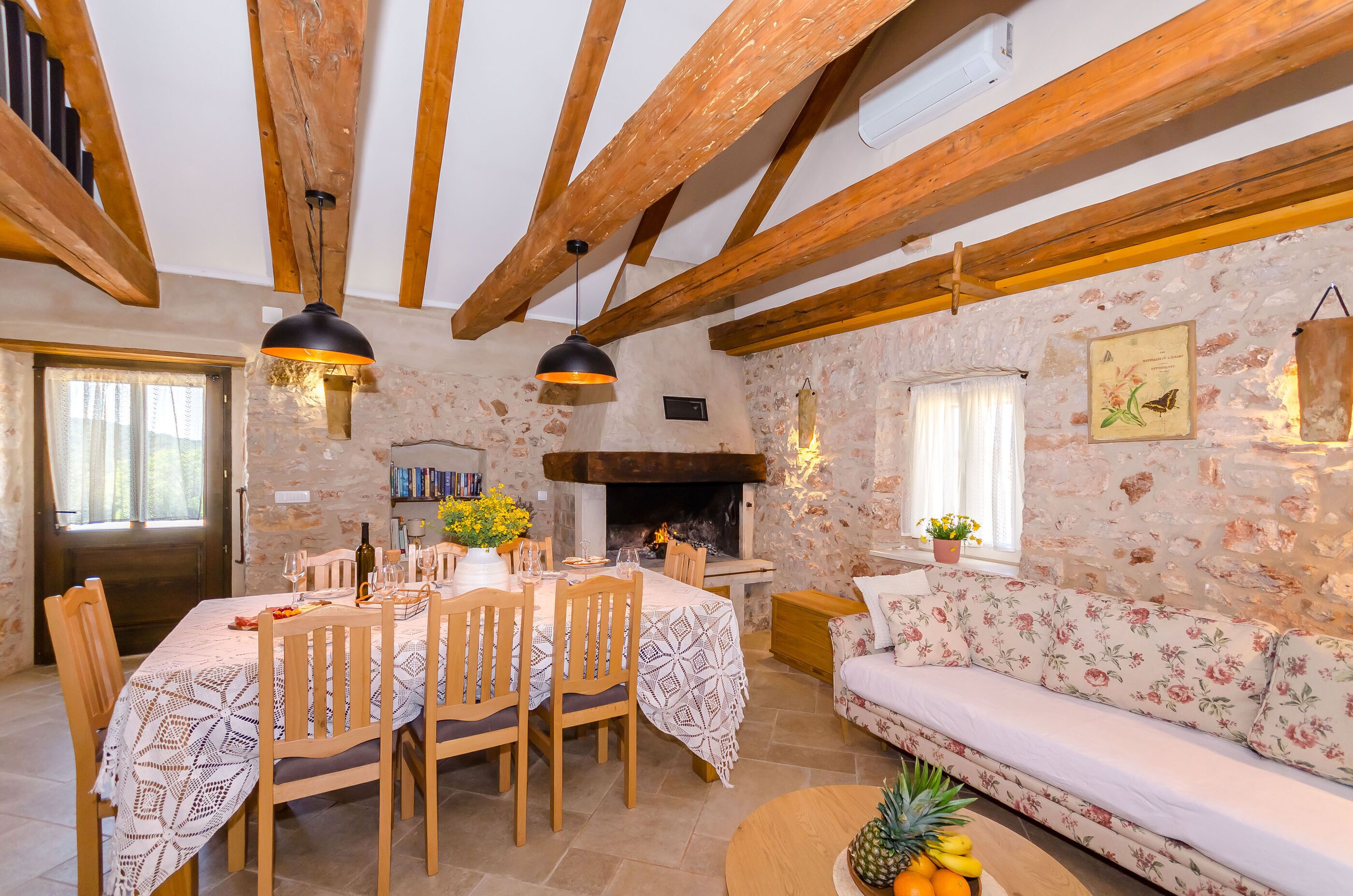 Un comedor rústico con pared de piedra, vigas de madera, chimenea y sofá.