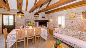 A rustic dining area with a stone wall, wooden beams, a fireplace, and a sofa. - House Bilusic (Jelsa)