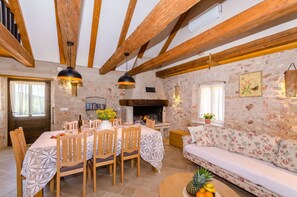A rustic dining area with a stone wall, wooden beams, a fireplace, and a sofa. - House Bilusic (Jelsa)