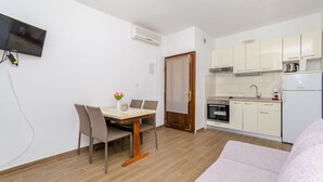 A modern kitchen with a built-in oven, a refrigerator, and a microwave. There is a dining area with a table and chairs, and a TV mounted on the wall. - Apartments Lida (Jelsa)