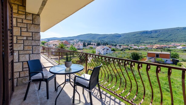 A balcony with a table and chairs, overlooking a rural landscape with houses and hills. - Apartments Lida (Jelsa)
