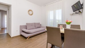 A modern living room with a sofa, dining table, chairs, a flat-screen TV, and a decorative mirror. - Apartments Lida (Jelsa)