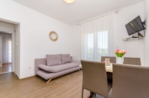 Ein modernes Wohnzimmer mit einer Couch, einem Esstisch, Stühlen, einem Flachbildfernseher und einem dekorativen Spiegel.