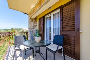 Ein Balkon mit zwei Korbstühlen, einem Glastisch und einem Blumentopf.