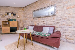 A room with a stone wall, a red sofa, a small round table, and a wooden cabinet. - Apartment Sealine One (Omis)
