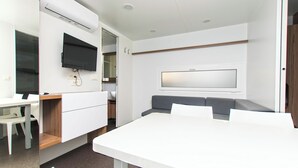Een moderne kamer met een witte tafel, een grijze bank, een flatscreen televisie aan de muur en een houten kast.