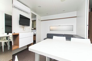 Ein modernes Zimmer mit einem weißen Tisch, einem grauen Sofa, einem flachbildfernseher an der Wand und einem Holzschrank.