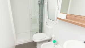 Een badkamer met een douchecabine, toilet, wastafel en spiegel boven de wastafel.