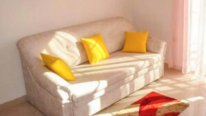 A beige sofa with yellow cushions, a red throw, and a painting on the wall. - Apartments Eden (Crikvenica)
