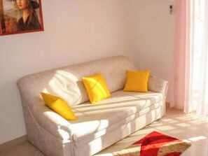 Ein beiges Sofa mit gelben Kissen, einer roten Decke und einem Bild an der Wand.