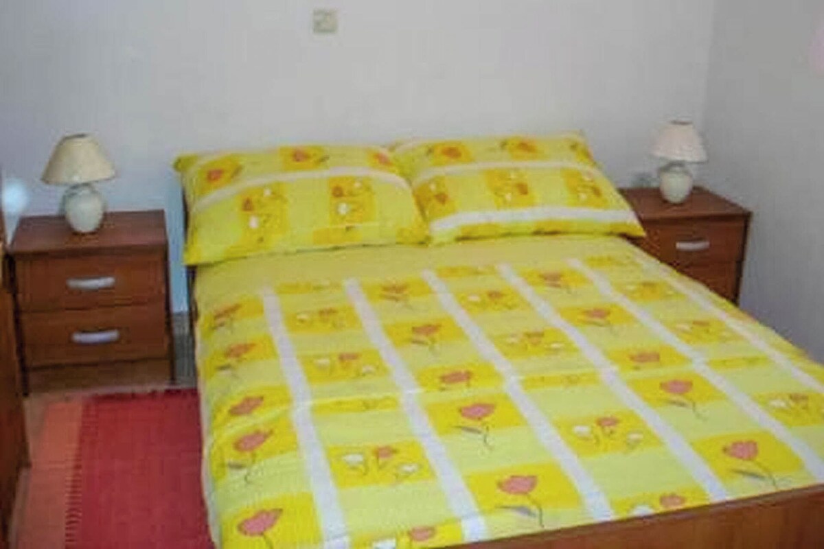 A bed with a yellow floral bedspread, two bedside tables with lamps, and a red rug.
