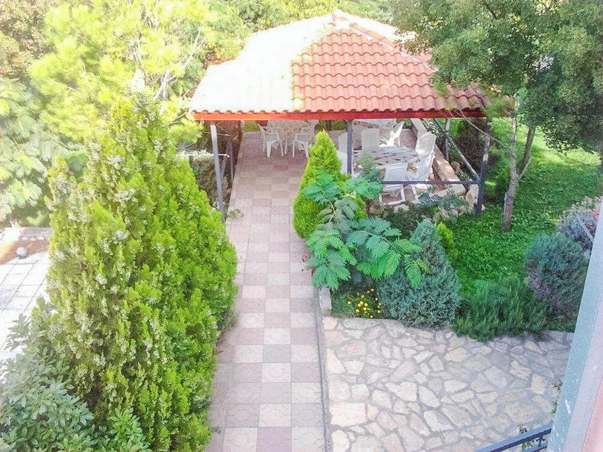 A covered outdoor seating area with stone flooring and surrounding greenery.