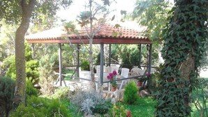 A covered outdoor seating area with tables and chairs, surrounded by greenery and trees. - Apartments Eden (Crikvenica)