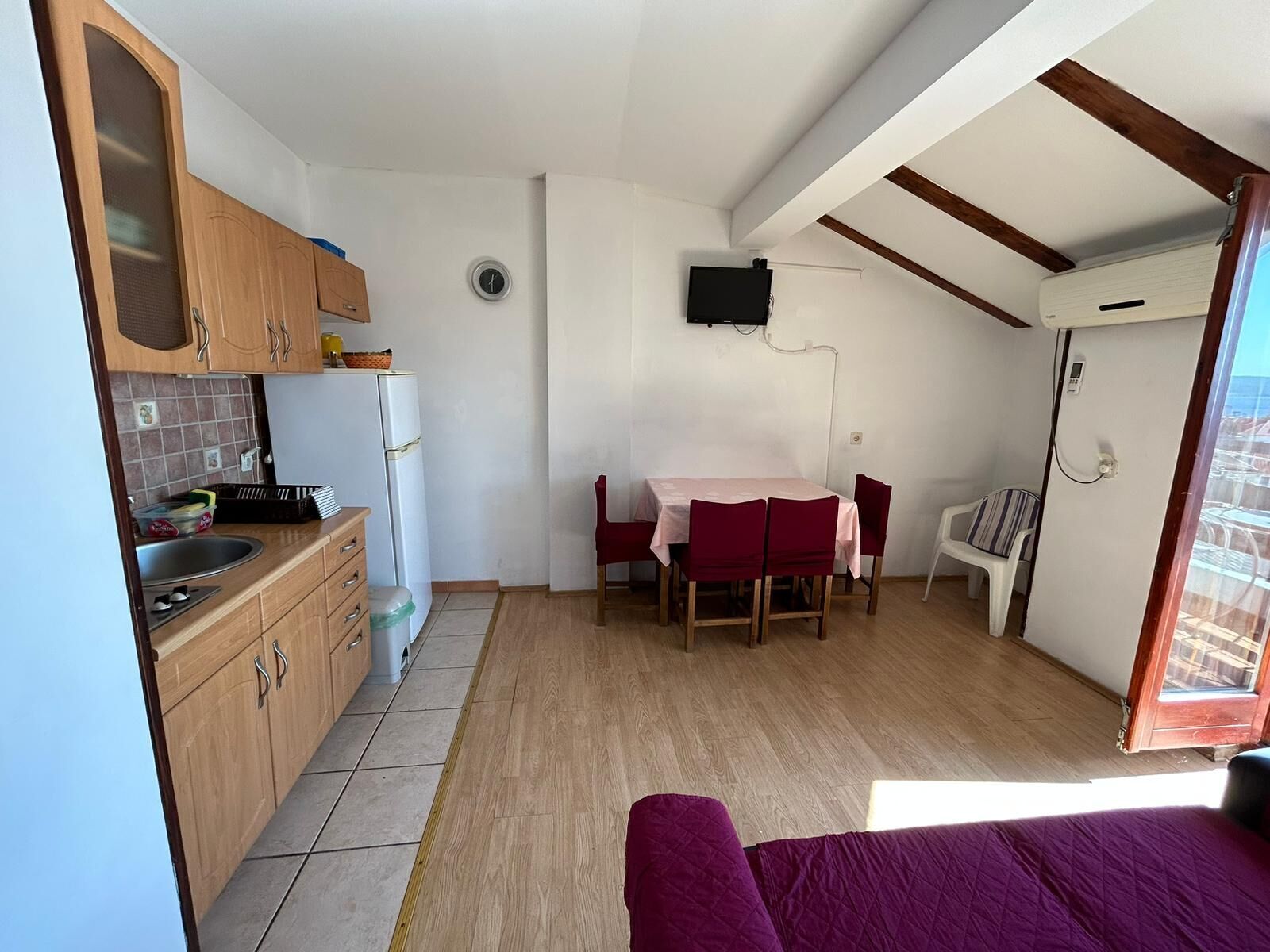 A compact kitchen with wooden cabinets, a refrigerator, and a dining area with a table and chairs.