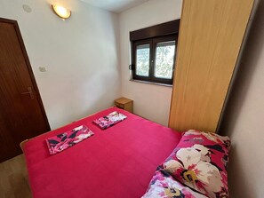 Ein kleines Zimmer mit Bett, Fenster, Tür und einer Lampe.