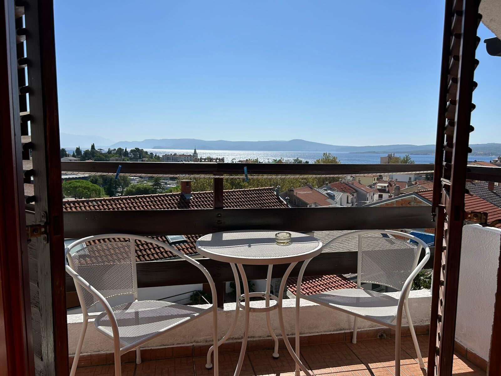 A balcony with a table and chairs, overlooking a cityscape and a body of water.