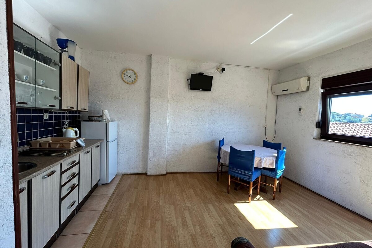 A compact kitchen with a dining area, a clock, and an air conditioning unit.
