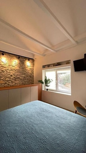 Une chambre avec un mur en pierre, une fenêtre avec une plante, un lit et une chaise.