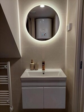 Un baño con un espejo redondo, un lavabo blanco y un perchero para toallas.
