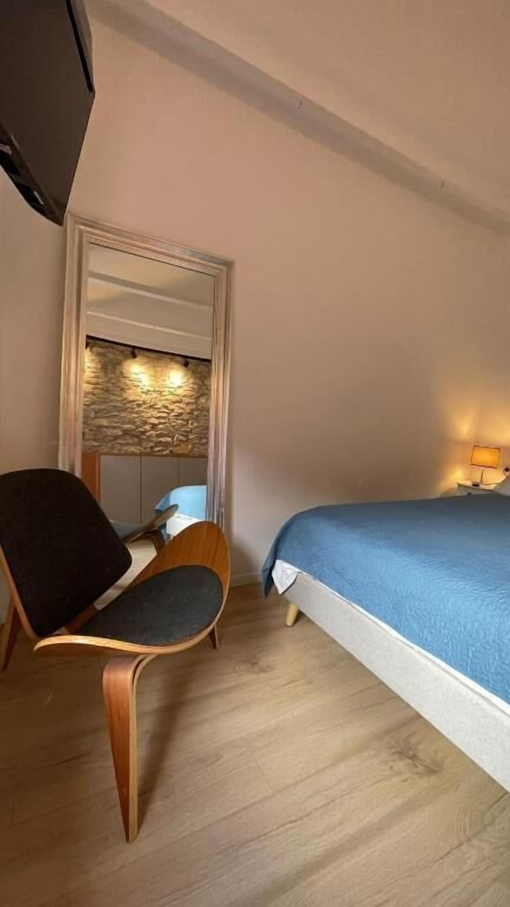Een hotelkamer met een bed, een stoel, een bureau, een televisie en een stenen muur.