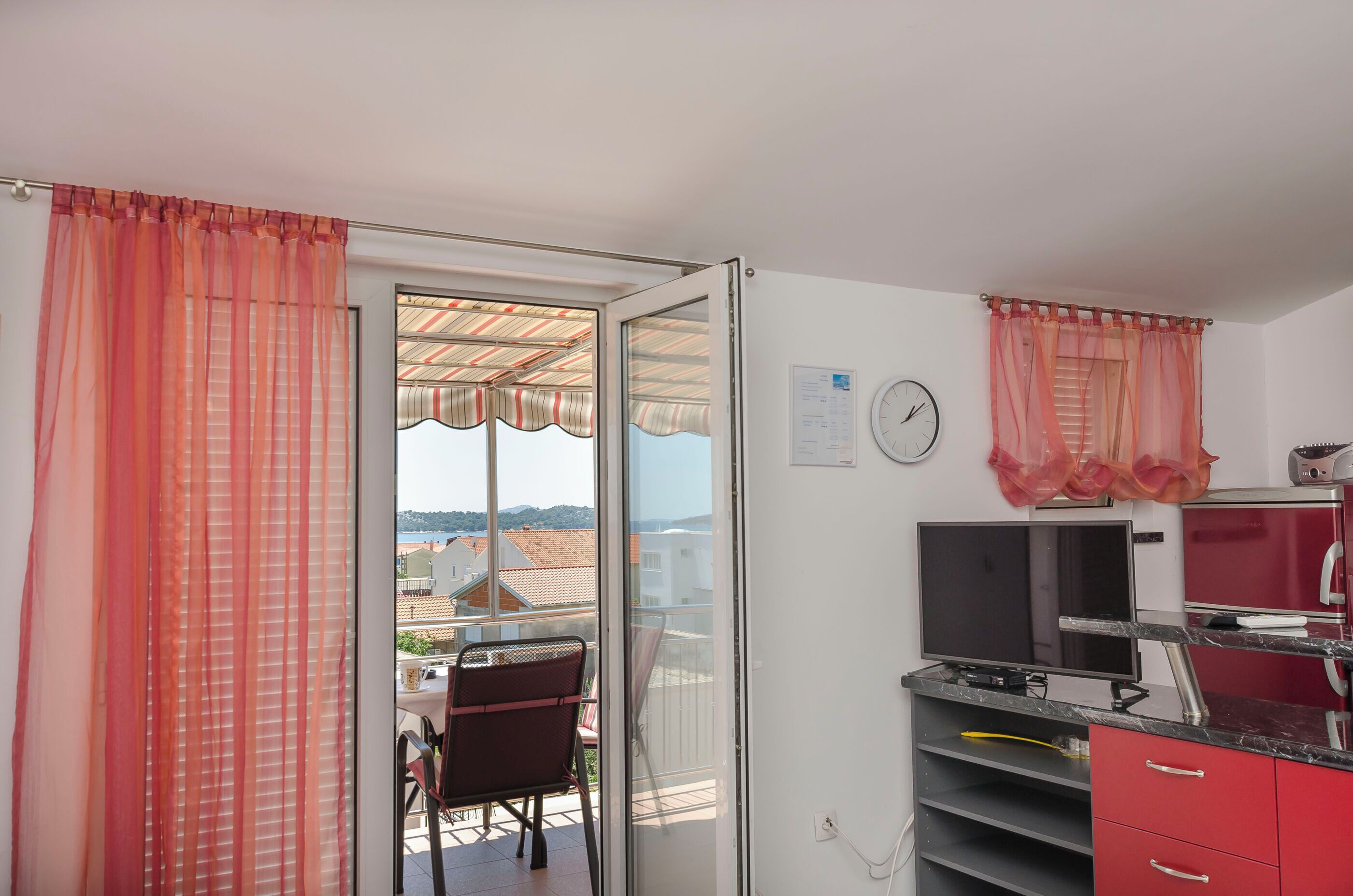 A room with a balcony, a TV, a clock, and a red cabinet.