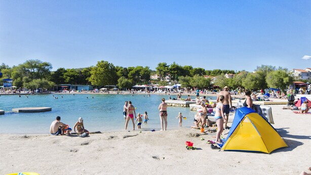 Ein Strand mit Menschen, einem Zelt und einem Schwimmbecken.
